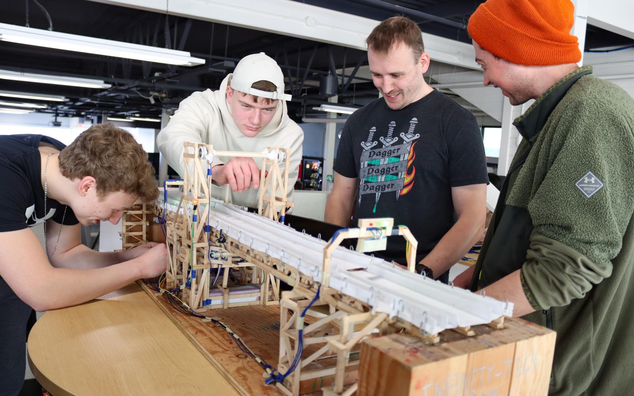 Four students bend over a bridge structure together