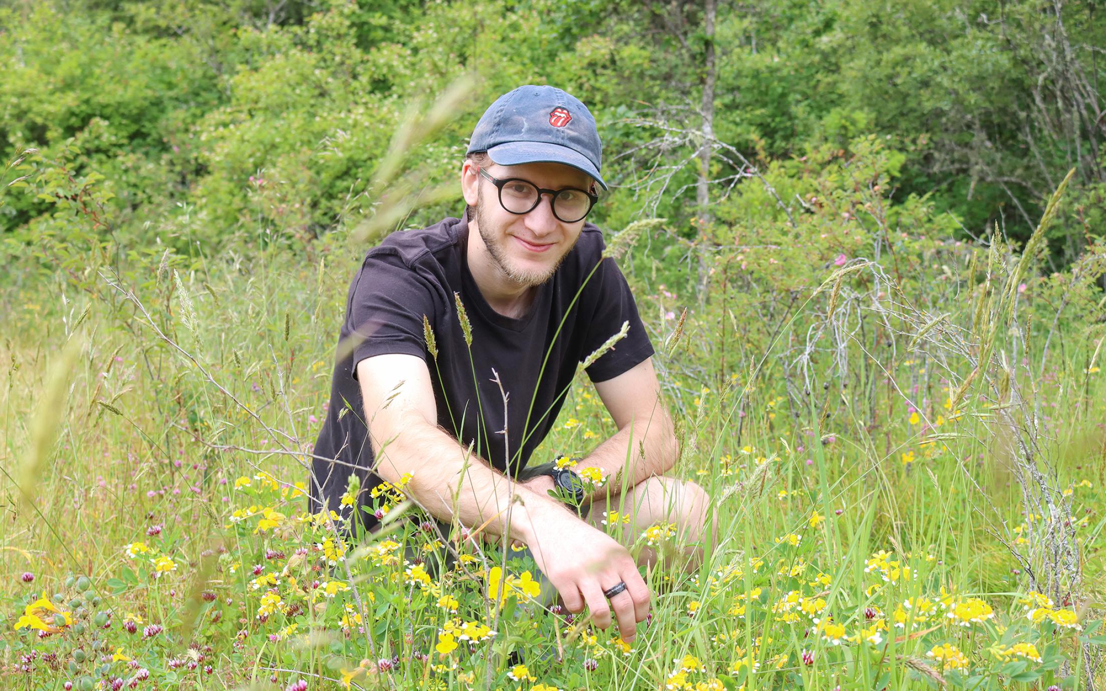Bryan Lamprecht kneels in front of a patch of Hosackia pinnata flowers nestled in a field of grass.