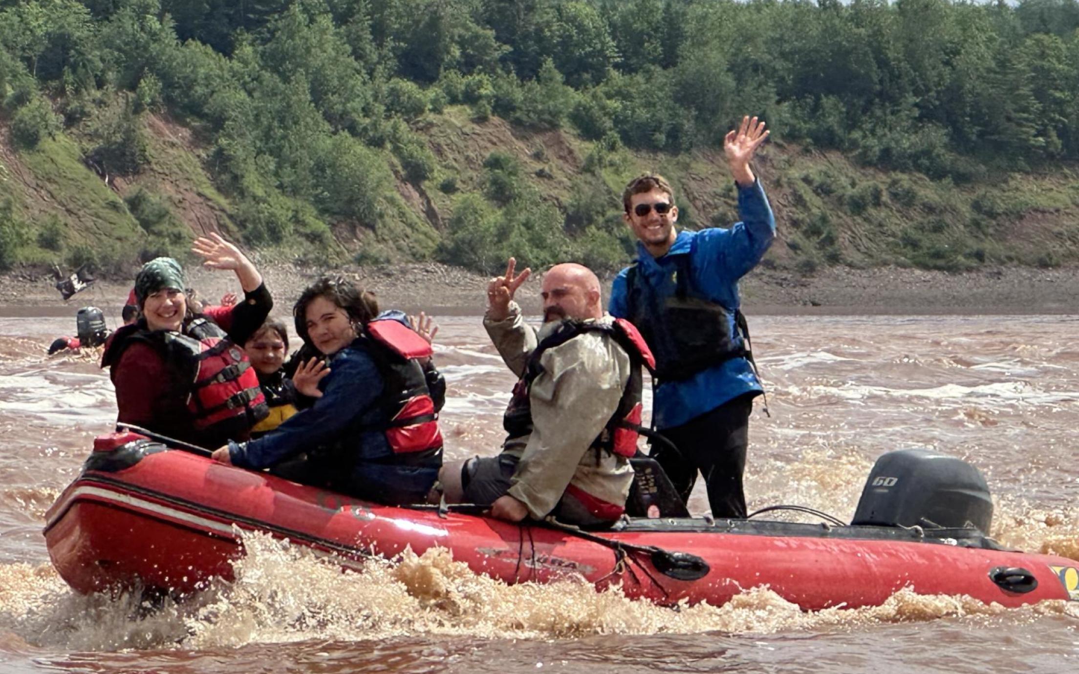 Lucas Gamp in a raft on a river with clients waving at the camera