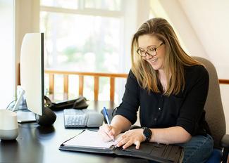 Woman writing at a desk by a window. 