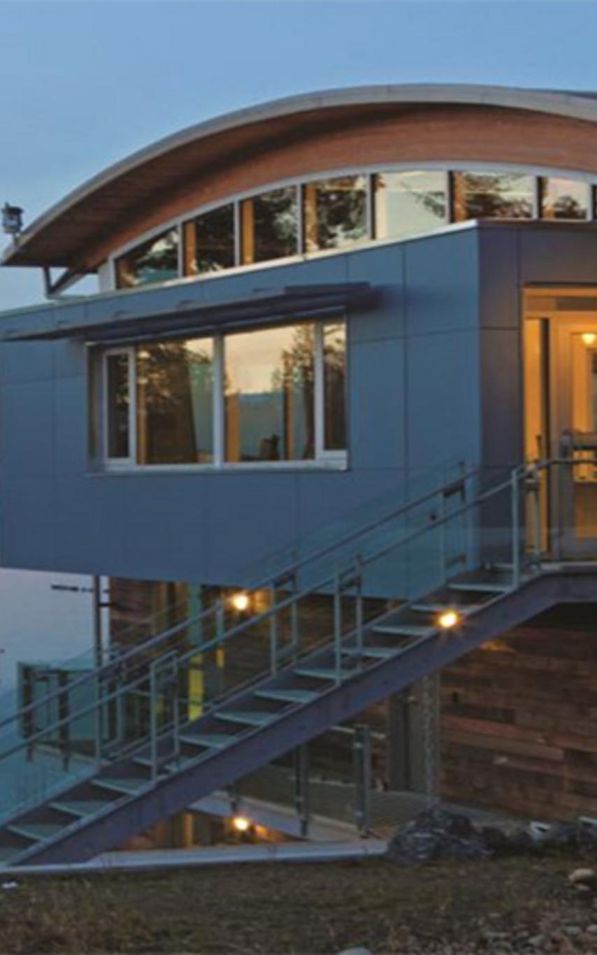 A modern looking building on the ocean at sunrise.